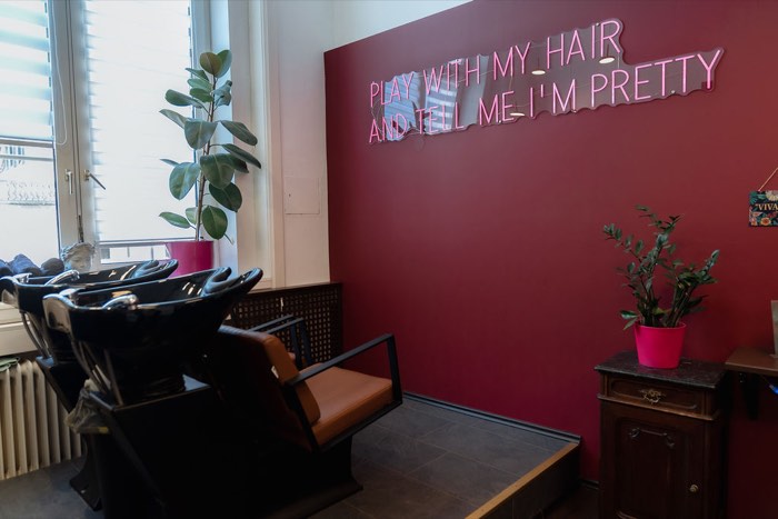 Waschbereich mit pinker Neonschrift „Play with my hair and tell me I'm pretty“ an bordeauxroter Wand