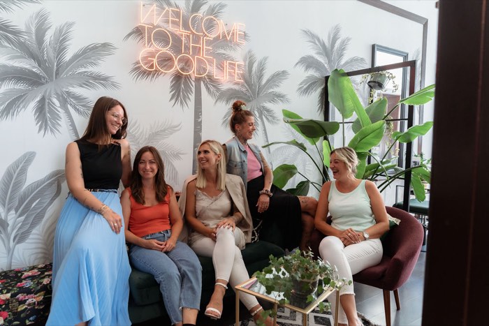 Das fünfköpfige Nu:Hair Team sitzt auf dem grünen Samtsofa unter der Neonschrift