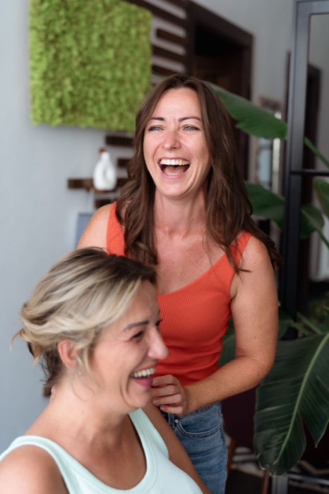 Zwei Stylistinnen von Nu:Hair lachen gemeinsam vor einer Mooswand